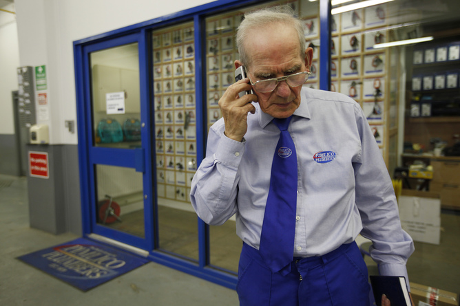 Depot Supervisor Eric Headley, 74, takes a call on his mobile phone while at work for Pimlico Plumbers in London July 29, 2010. Britain announced plans to scrap the fixed retirement age next year, saying it wanted to give people the chance to work beyond 65, but business leaders warned the move would create serious problems. REUTERS/Suzanne Plunkett (BRITAIN - Tags: POLITICS SOCIETY) - RTR2GUL1